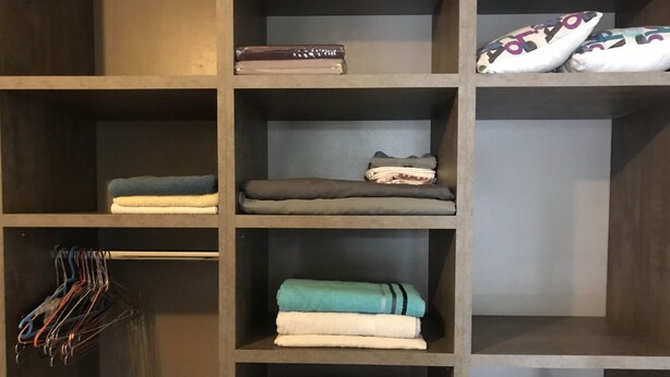 A storage unit with shelves containing folded towels, a rolled-up blanket, and a pair of slippers.
