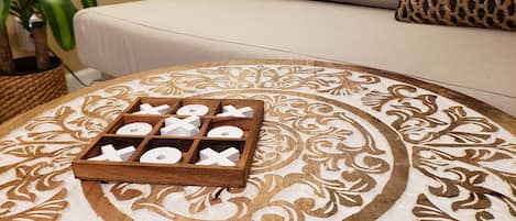 A wooden tray with cut-out letters on a patterned tablecloth, placed on a round table in a room with a beige sofa and a woven basket.