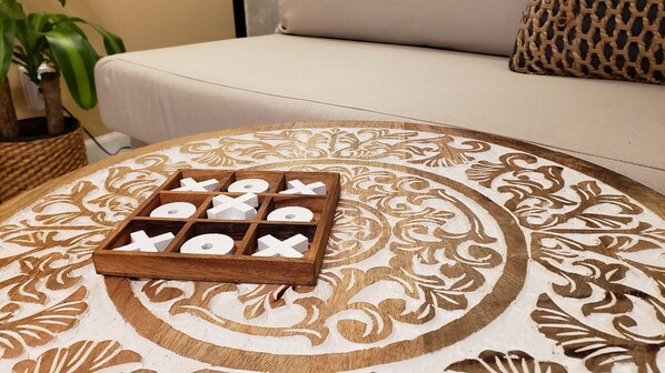 A wooden tray with cut-out letters on a patterned tablecloth, placed on a round table in a room with a beige sofa and a woven basket.