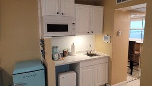 A compact kitchen with white cabinets, a microwave, a small refrigerator, and a sink. - Oceanfront Building Studio Queen Bed Smart TV Pool (Daytona Beach)