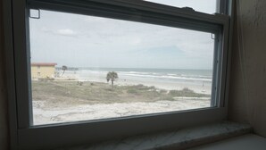 A window with a view of a beach and a building in the distance. - Oceanfront Building Studio Queen Bed Smart TV Pool (Daytona Beach)