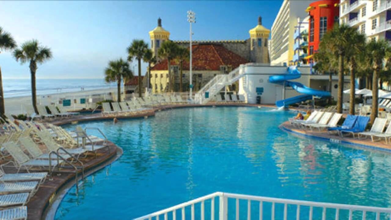 Una piscina con lettini e uno scivolo acquatico, circondata da palme e un edificio con cupole gialle.