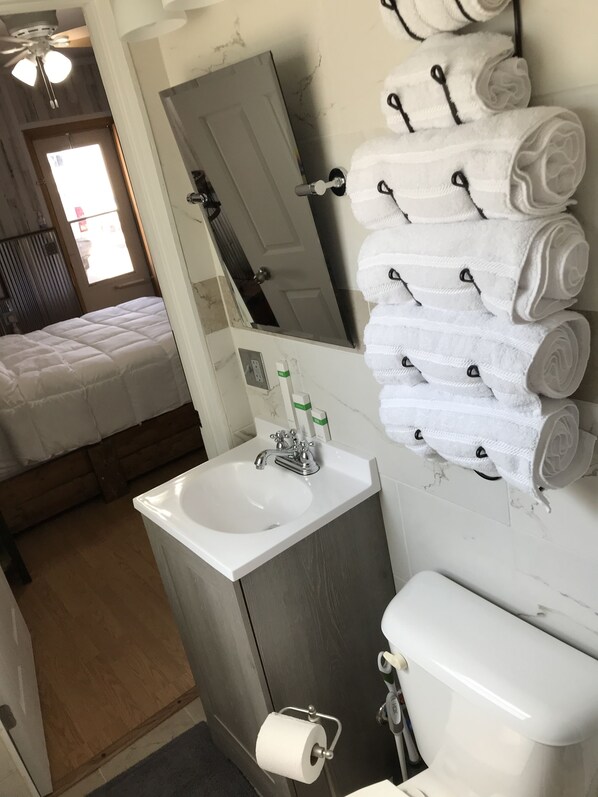 A bathroom with a sink, toilet, and a mirror. There are towels stacked on a rack. - Sunrise Room (Moorcroft)