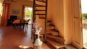 A spacious room with a spiral staircase, a dining area with a table and chairs, and a large window providing a view of the outdoors. - Lemon's house by the sea (Sicilia)