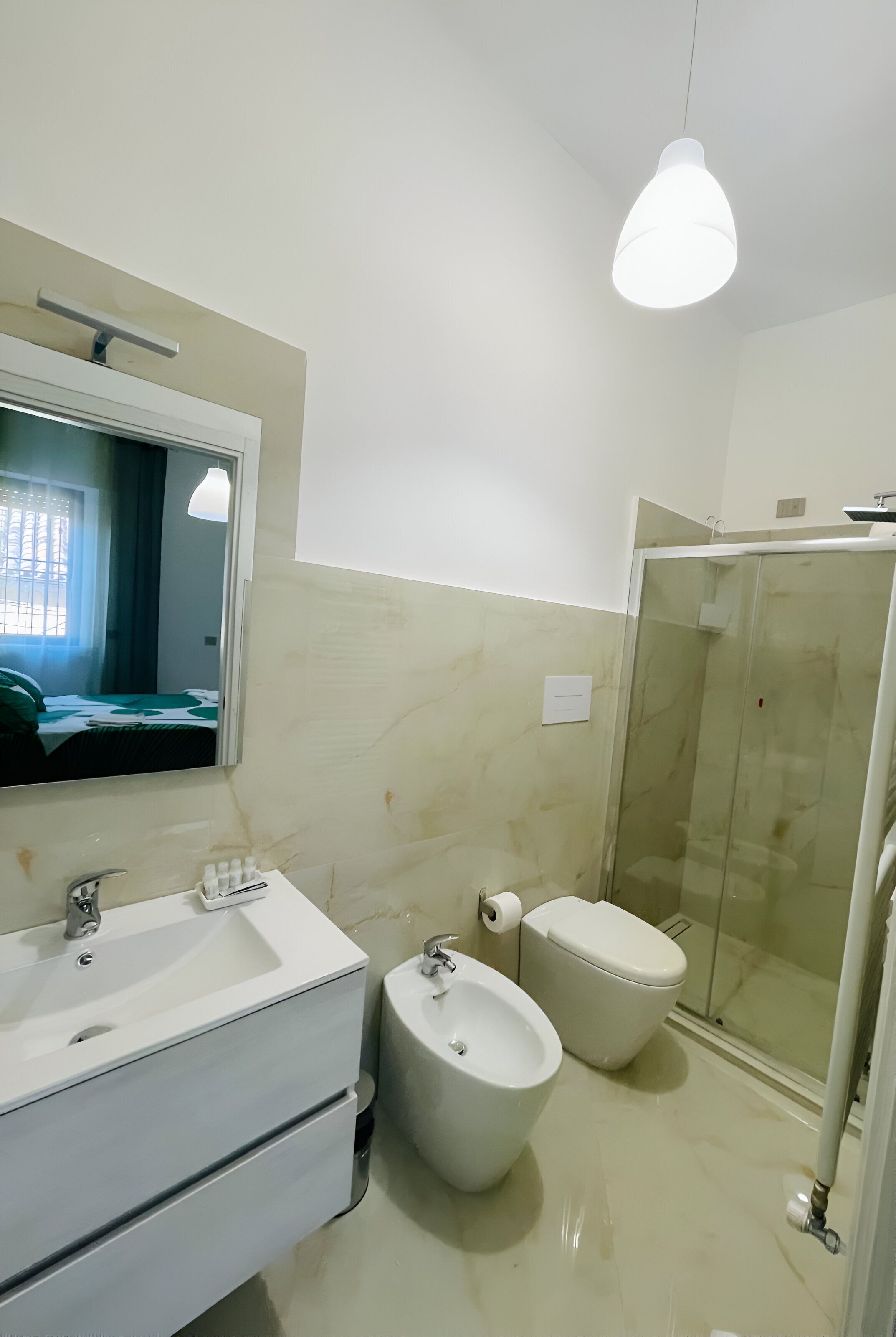A modern bathroom with a large mirror, two sinks, a bidet, and a glass-enclosed shower.