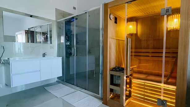 A modern bathroom with a glass shower enclosure, a wooden sauna, and a white vanity with a mirror.