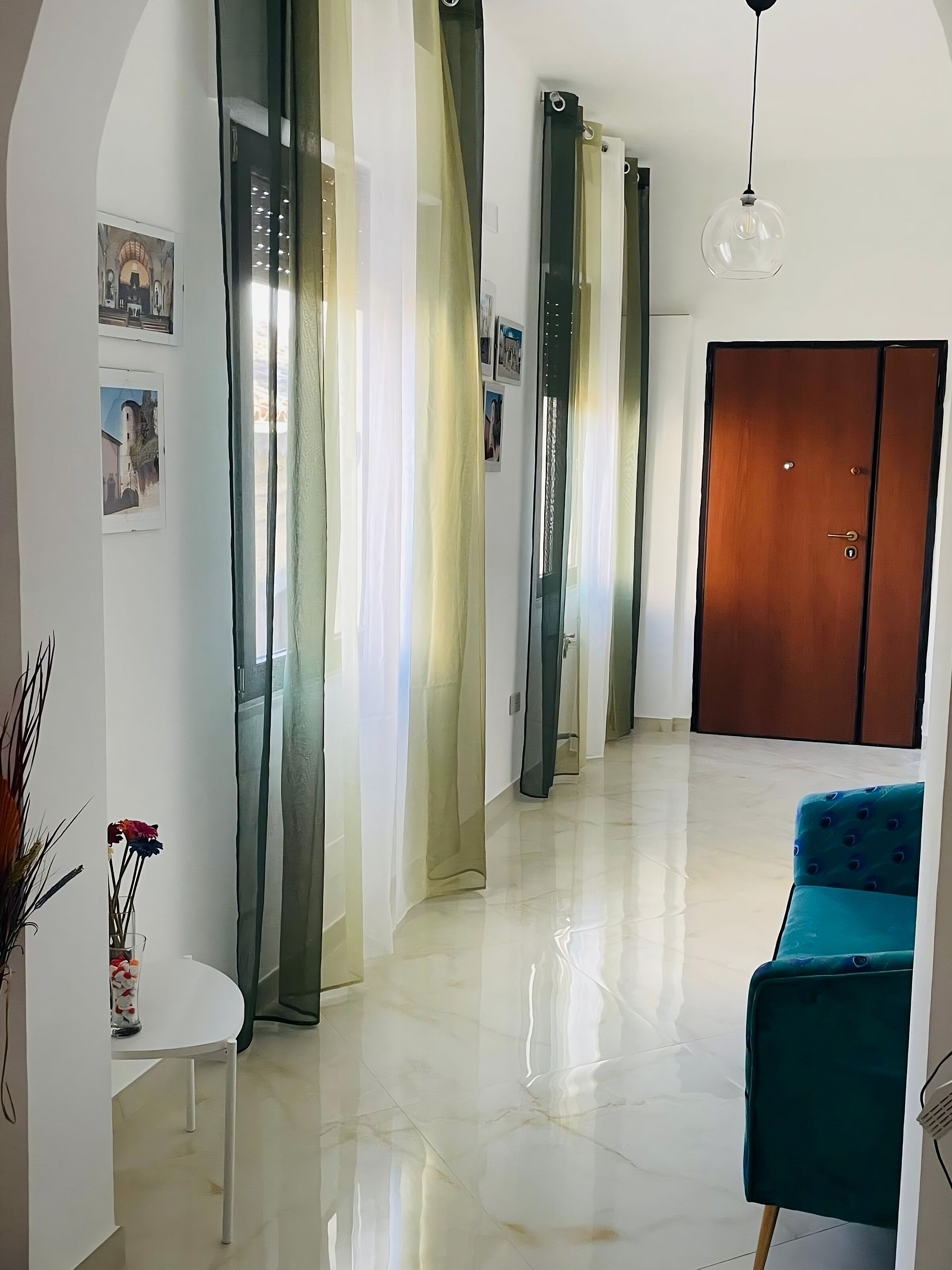 Un pasillo espacioso con una puerta de madera, una silla azul y una mesa blanca con un florero.