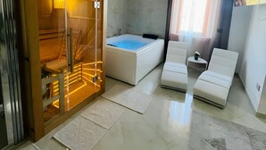 A modern bathroom with a bathtub, a glass-enclosed sauna, and two white chairs.