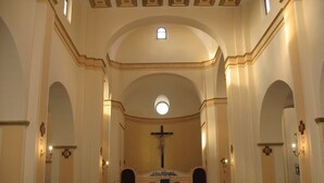 A church interior with wooden pews, a central altar with a cross, and a dome-shaped ceiling.