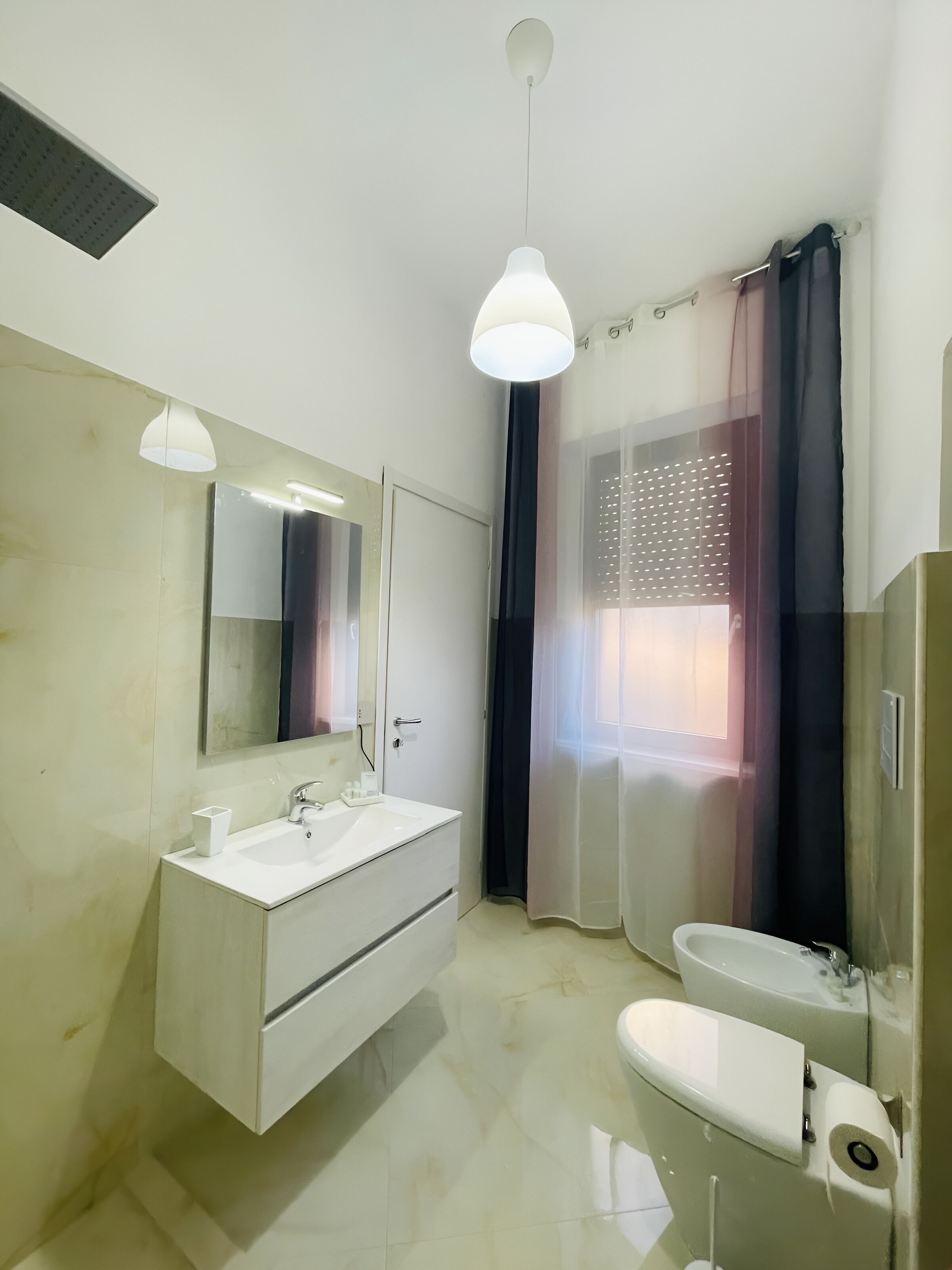 Une salle de bain moderne avec un meuble-lavabo blanc, un grand miroir, des toilettes et un espace douche séparé par un rideau.