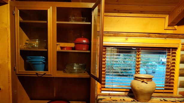 A wooden interior with a cabinet containing dishes and a window with blinds. - Cozy Log Cabin in peaceful wooded surroundings (Monroe)