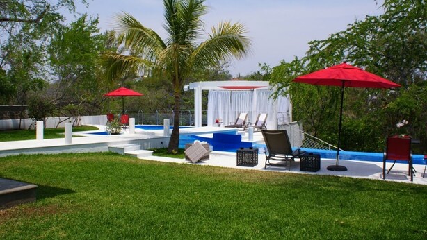 Un espace piscine avec des chaises longues, des parasols rouges et un coin salon abrité.