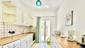 Una cocina compacta con armarios blancos, lavadora, cafetera y tostadora.