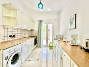A compact kitchen with white cabinets, a washing machine, a coffee maker, and a toaster.
