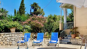 Zona de piscina con sillas reclinables azules, un muro de piedra y una escalera que lleva a un nivel superior.