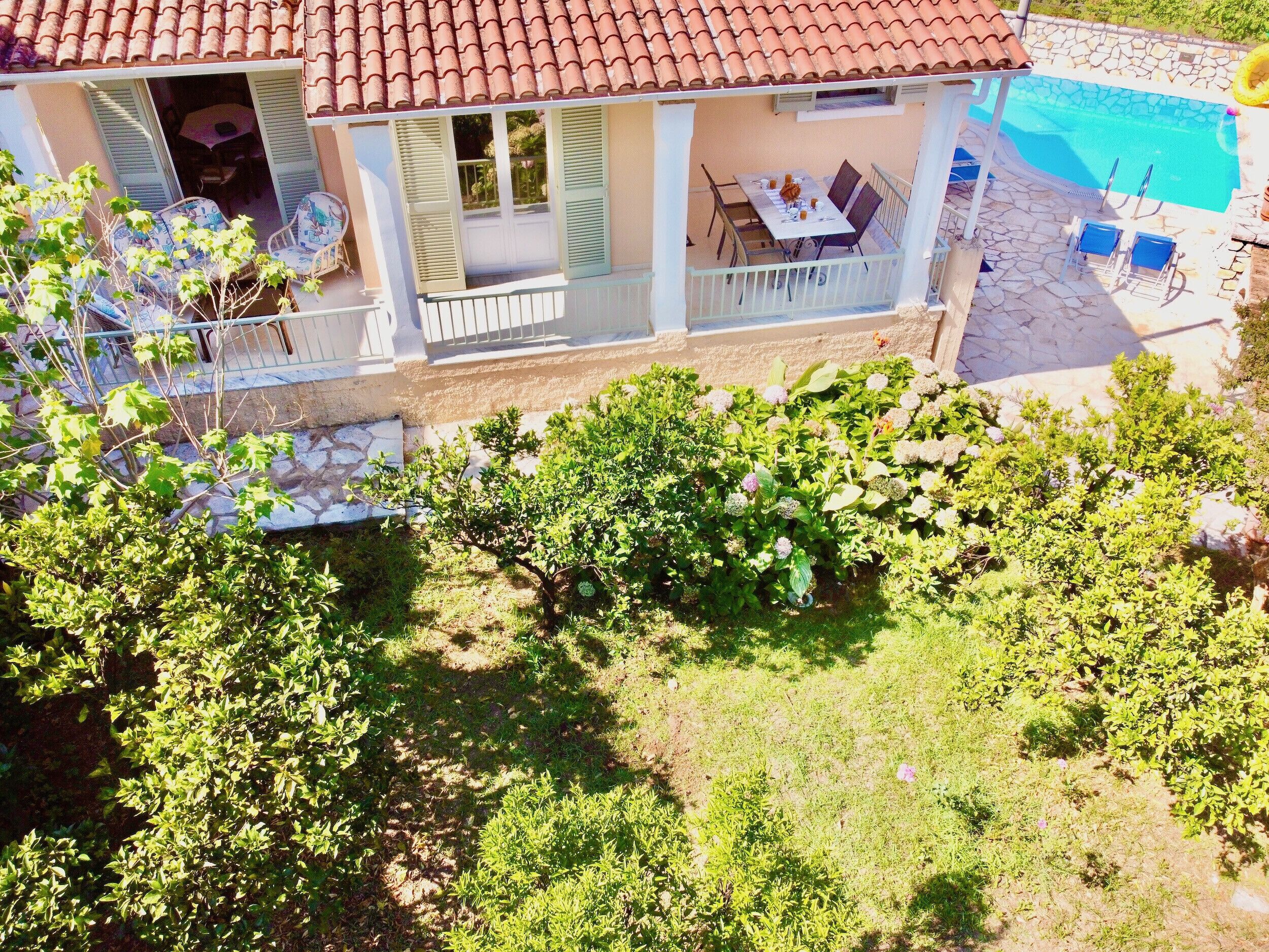 Ein zweistöckiges Haus mit Balkon, der auf einen Swimmingpool mit üppiger Bepflanzung blickt.