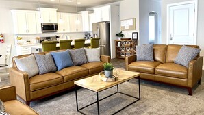 Ein modernes Wohnzimmer mit einer braunen Ledersofa-Garnitur, einem Holztisch und einer Küche im Hintergrund.