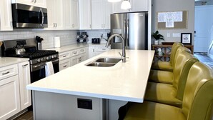Eine moderne Küche mit weißen Schränken, Edelstahlgeräten, einer zentralen Kochinsel mit Spüle und einem gelben Ledersofa.