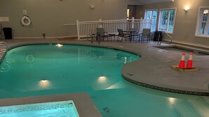 An indoor swimming pool with a tiled edge, a lifeguard chair, and a small seating area with tables and chairs. - Quiet resort condo close to Goose Rocks beach (Kennebunkport)