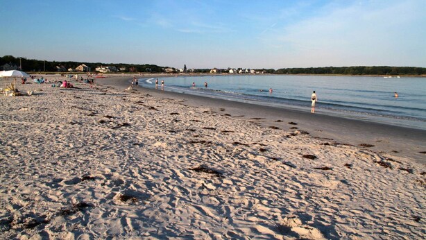 A sandy beach with footprints, a few umbrellas, and houses in the background. - Quiet resort condo close to Goose Rocks beach (Kennebunkport)