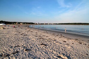 A sandy beach with footprints, a few umbrellas, and houses in the background.