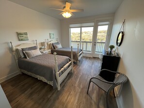 Two single beds with wooden headboards, a ceiling fan, and a large window with a view of the surrounding landscape.
