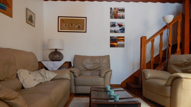A living room with a brown sofa, a beige armchair, and a wooden staircase.