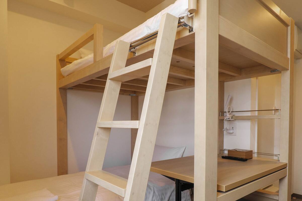 Una cama litera con una escalera, un escritorio y una silla en una habitación con piso alfombrado y un equipo de aire acondicionado en la pared.