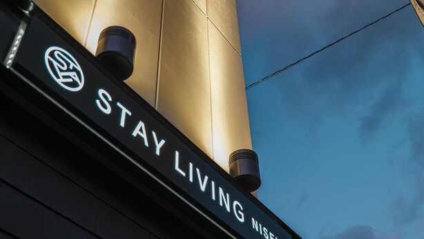 A sign with the text "STAY LIVING NISEKO" against a building facade.