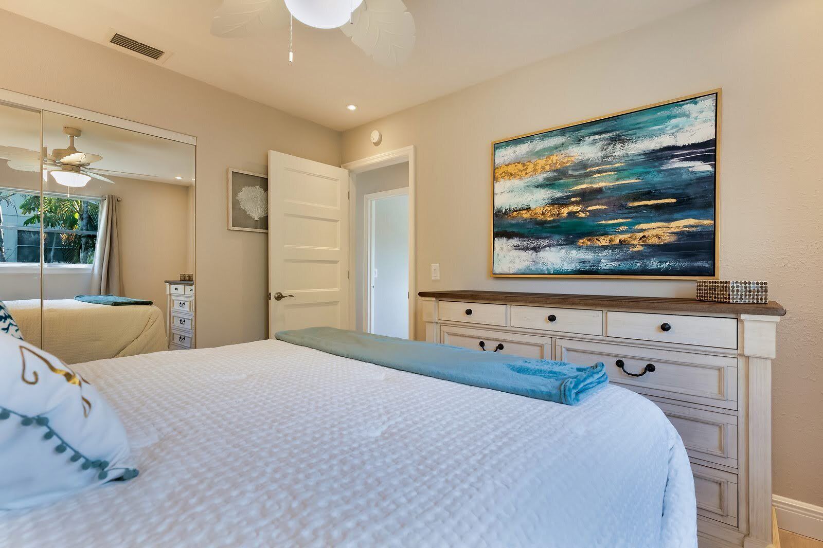 Un dormitorio con cama, cómoda, un cuadro y ventilador de techo.