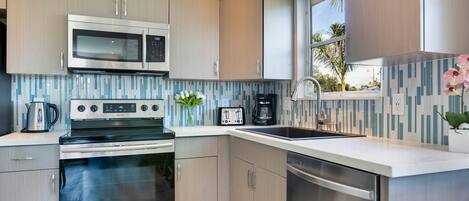 A modern kitchen with stainless steel appliances, a built-in microwave, a coffee maker, and a window with a view of palm trees.