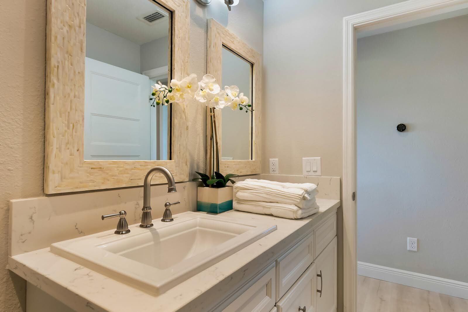A bathroom with a white sink, two mirrors, and a plant.