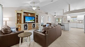 A modern living room with a large flat-screen TV, leather sofas, a small round table, and a ceiling fan. - Heated saltwater pool, newly furnished - Villa Tropical Paradise. (Cape Coral)