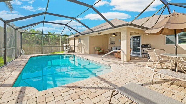 A covered outdoor swimming pool with a patio area, lounge chairs, and a barbecue setup. - Heated saltwater pool, newly furnished - Villa Tropical Paradise. (Cape Coral)