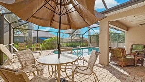 An outdoor patio with a glass enclosure, a pool, wicker furniture, and a large umbrella. - Heated saltwater pool, newly furnished - Villa Tropical Paradise. (Cape Coral)