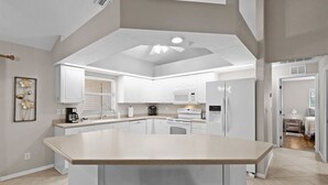 A modern kitchen with white cabinets, a central island, and a dining area with two chairs. - Heated saltwater pool, newly furnished - Villa Tropical Paradise. (Cape Coral)
