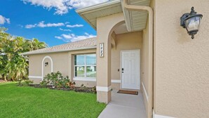 A single-story house with a beige exterior, a white door, and a small porch area. - Heated saltwater pool, newly furnished - Villa Tropical Paradise. (Cape Coral)