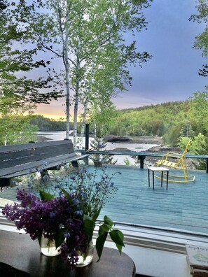 Una terraza de madera con un banco y una mesa, con vista a un río y un área boscosa.