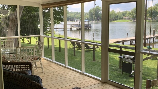 Una terraza techada con muebles de mimbre y vistas a un lago con un muelle y un bote.