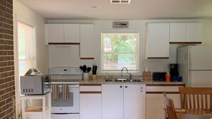 Cocina compacta con armarios blancos, horno empotrado, microondas, lavamanos y ventana con persianas.