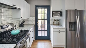 Une cuisine avec des armoires blanches, un réfrigérateur en acier inoxydable, un four à micro-ondes, une cuisinière à gaz et une porte bleue.