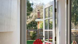 Une porte donnant sur un patio où se trouve un fauteuil Adirondack rouge et un sol en briques.