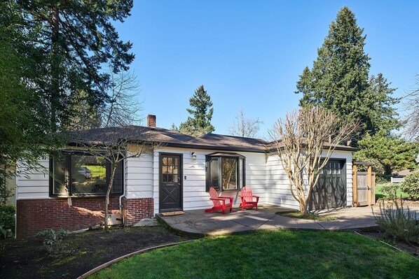 A single-story house with a front porch, two red Adirondack chairs, a brick foundation, and a covered patio area. - U Of O ▪️ HOT TUB ▪️ FIRE PITS ▪️ GOLF (Eugene)