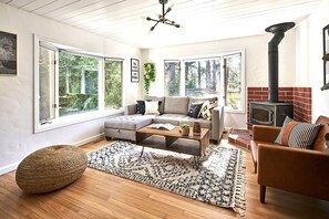 Ein gemütliches Wohnzimmer mit einer Eckcouch, einem Couchtisch, einem Kamin und großen Fenstern mit Blick ins Freie.
