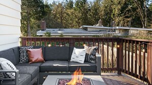 Une terrasse extérieure avec un foyer, un canapé gris agrémenté de coussins à motifs et une rambarde en bois.