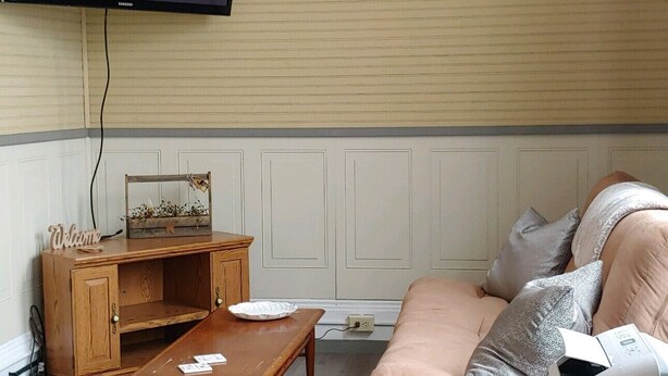Ein Wohnzimmer mit an der Wand montiertem Fernseher, einer Holzkommode, einem Sofa, einem Couchtisch und einer Waschmaschine.