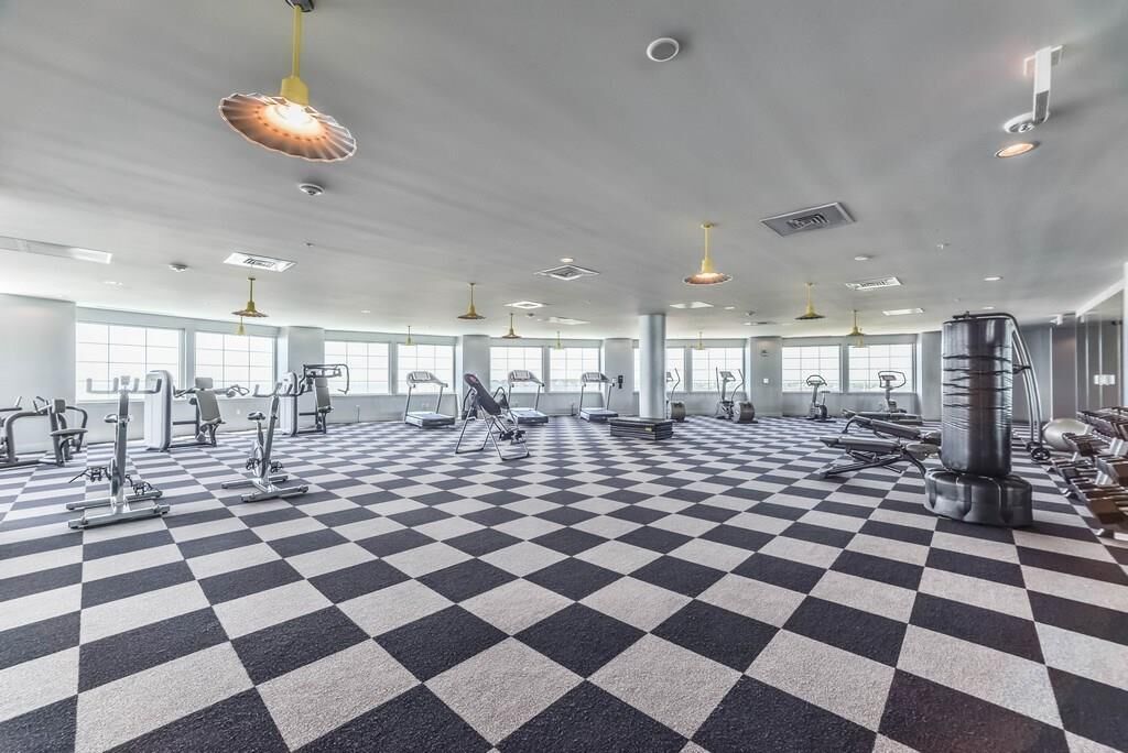 Un gimnasio con piso a cuadros, diverso equipo de ejercicio y ventanas amplias.