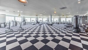 Ein Fitnessraum mit Schachbrettmuster-Boden, verschiedenen Trainingsgeräten und großen Fenstern.