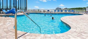 A swimming pool with clear blue water, surrounded by lounge chairs and a tiled deck.