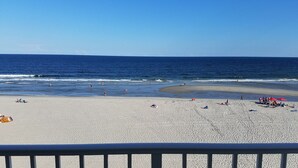 Een strand met helder uitzicht op de oceaan, mensen die langs de kust wandelen en strandparasols.